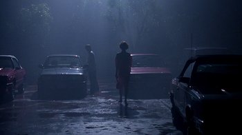 Movie still from “Pretty in Pink” (1986), directed by Howard Deutch – Two people standing in the rain next to parked cars; Wide shot, Low angle