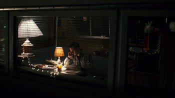 Movie still from “Pride and Glory” (2008), directed by Gavin O'Connor – A man sitting in front of a lamp on a table; Wide shot, High angle