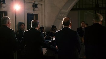 Movie still from “Pride and Glory” (2008), directed by Gavin O'Connor – Two men in suits are speaking into microphones in front of a crowd; Medium shot, Over the shoulder angle