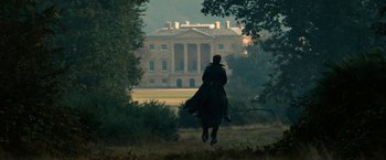 Movie still from “Pride and Prejudice and Zombies” (2016), directed by Burr Steers – A person riding a horse in a field near a building; Extreme Wide shot, Low angle