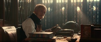 Movie still from “Pride and Prejudice and Zombies” (2016), directed by Burr Steers – An older man sitting at a table with a cat; Medium shot, Low angle