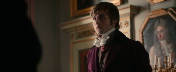 Movie still from “Pride and Prejudice and Zombies” (2016), directed by Burr Steers – A young man in a purple jacket and a white bow tie standing in front of a fireplace; Medium shot, Over the shoulder angle