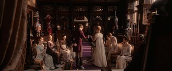 Movie still from “Pride and Prejudice and Zombies” (2016), directed by Burr Steers – A group of people sitting in a room with a man and woman; Wide shot, Over the shoulder angle