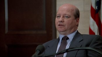 Movie still from “Primal Fear” (1996), directed by Gregory Hoblit – A man in a suit and tie is speaking at a podium; Close Up shot, Over the shoulder angle