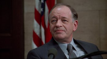 Movie still from “Primal Fear” (1996), directed by Gregory Hoblit – A man in a suit and tie sitting in front of an american flag; Close Up shot, Low angle