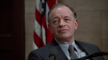 Movie still from “Primal Fear” (1996), directed by Gregory Hoblit – A man in a suit and tie in front of an american flag; Close Up shot, Low angle