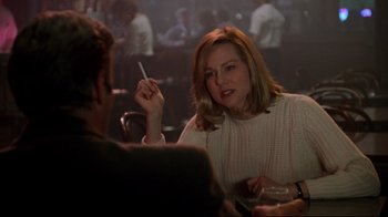 Movie still from “Primal Fear” (1996), directed by Gregory Hoblit – A woman sitting in front of a man holding a cigarette in her mouth; Medium shot, Over the shoulder angle