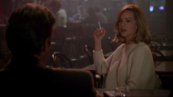 Movie still from “Primal Fear” (1996), directed by Gregory Hoblit – A woman sitting at a table holding a cigarette in front of a man; Medium shot, Over the shoulder angle