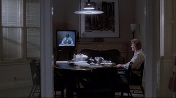 Movie still from “Primal Fear” (1996), directed by Gregory Hoblit – A man sitting at a table in front of a television; Wide shot, Over the shoulder angle