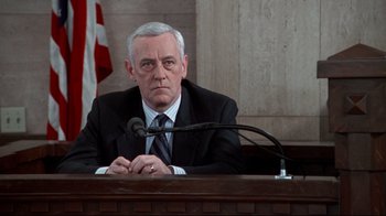 Movie still from “Primal Fear” (1996), directed by Gregory Hoblit – An older man sitting at a table in a courtroom; Medium shot, Low angle