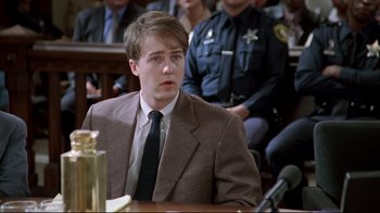 Movie still from “Primal Fear” (1996), directed by Gregory Hoblit – A man sitting in front of a microphone in a courtroom; Medium shot, Low angle
