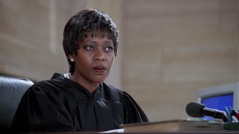 Movie still from “Primal Fear” (1996), directed by Gregory Hoblit – A woman wearing a black robe is sitting in front of a microphone; Close Up shot, Low angle