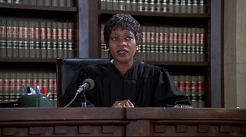Movie still from “Primal Fear” (1996), directed by Gregory Hoblit – A woman in a courtroom with a microphone; Medium shot, Low angle