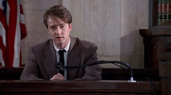 Movie still from “Primal Fear” (1996), directed by Gregory Hoblit – A man sitting at a table in front of a microphone; Medium shot, Low angle