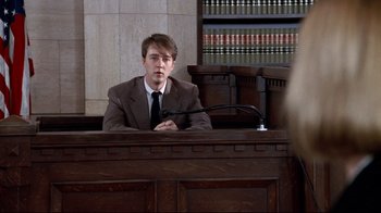 Movie still from “Primal Fear” (1996), directed by Gregory Hoblit – A man sitting in front of a microphone in a court room; Medium shot, Over the shoulder angle