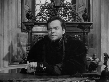 Movie still from “Prince of Foxes” (1949), directed by Henry King – Black and white photograph of a man sitting in a chair; Medium shot, High angle