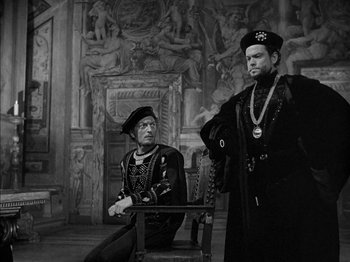 Movie still from “Prince of Foxes” (1949), directed by Henry King – Two men dressed in medieval garb sitting in front of a mural; Medium shot, High angle