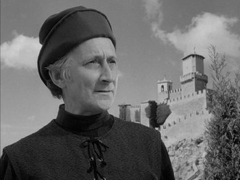 Movie still from “Prince of Foxes” (1949), directed by Henry King – An older woman wearing a hat standing in front of a castle; Medium shot, Low angle