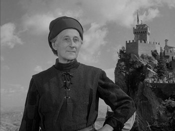 Movie still from “Prince of Foxes” (1949), directed by Henry King – An older woman wearing a hat standing in front of a castle; Medium shot, Low angle
