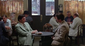 Movie still from “Prince of the City” (1981), directed by Sidney Lumet – Two men sitting at a table in front of a door; Wide shot, Over the shoulder angle
