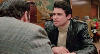 Movie still from “Prince of the City” (1981), directed by Sidney Lumet – A man sitting at a table talking to another man; Medium shot, Over the shoulder angle