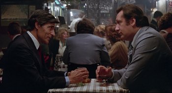 Movie still from “Prince of the City” (1981), directed by Sidney Lumet – Two men sitting at a table with a glass of red wine; Medium shot, Over the shoulder angle