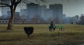 Movie still from “Prince of the City” (1981), directed by Sidney Lumet – A person sitting on a park bench in a field; Extreme Wide shot, High angle