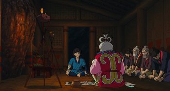 Movie still from “Princess Mononoke” (1997), directed by Hayao Miyazaki – An animated scene of a man sitting in front of an older woman; Wide shot, High angle