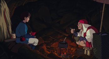 Movie still from “Princess Mononoke” (1997), directed by Hayao Miyazaki – A couple of people sitting in front of a fire pit; Wide shot, High angle