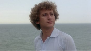 Movie still from “Prom Night” (1980), directed by Paul Lynch – A young man with curly brown hair looks into the distance while wearing a white shirt; Close Up shot, Low angle