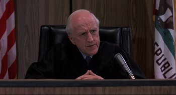 Movie still from “Psycho II” (1983), directed by Richard Franklin – An older man sitting in front of a microphone in a courtroom; Close Up shot, High angle