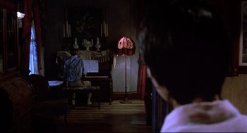 Movie still from “Psycho II” (1983), directed by Richard Franklin – A man sitting in front of a piano in a living room; Wide shot, High angle