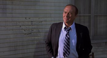 Movie still from “Psycho II” (1983), directed by Richard Franklin – A man in a suit and tie standing in front of a building; Medium shot, Low angle