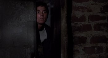 Movie still from “Psycho II” (1983), directed by Richard Franklin – A man standing in a dark room looking at the camera; Close Up shot, Low angle