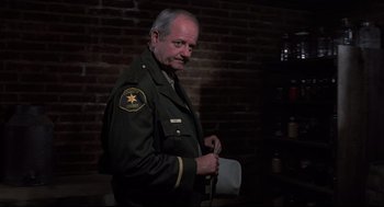 Movie still from “Psycho II” (1983), directed by Richard Franklin – A man in a sheriff uniform holding a whip; Medium shot, Low angle