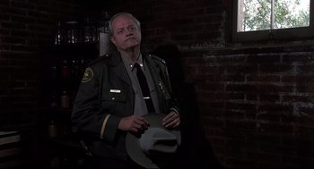 Movie still from “Psycho II” (1983), directed by Richard Franklin – A man in uniform holding a hat in a dark room; Medium shot, Low angle