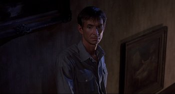 Movie still from “Psycho II” (1983), directed by Richard Franklin – A man standing in a room with a light on his face; Medium shot, Over the shoulder angle