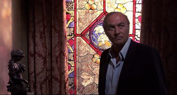 Movie still from “Psycho II” (1983), directed by Richard Franklin – A man standing in front of a stained glass window; Medium shot, Low angle