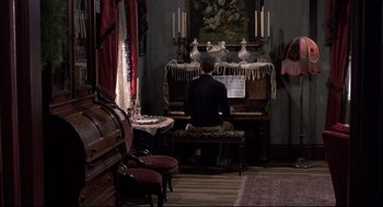 Movie still from “Psycho II” (1983), directed by Richard Franklin – A man sitting in front of a piano in a living room; Wide shot, High angle