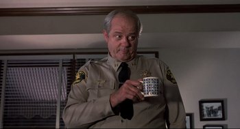 Movie still from “Psycho II” (1983), directed by Richard Franklin – A police officer holding a coffee mug in his hand; Medium shot, Low angle