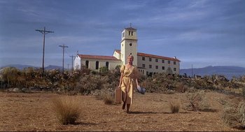 Movie still from “Psycho III” (1986), directed by Anthony Perkins – An older woman in a dress walking in front of an old church; Extreme Wide shot, Low angle