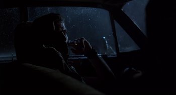 Movie still from “Psycho III” (1986), directed by Anthony Perkins – A man sitting in the driver's seat of a car while smoking a cigarette; Medium shot, Low angle