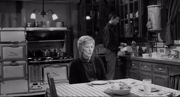 Movie still from “Psycho III” (1986), directed by Anthony Perkins – An older woman sitting at a table in a kitchen; Medium shot, Over the shoulder angle