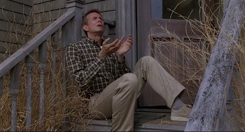 Movie still from “Psycho III” (1986), directed by Anthony Perkins – A man sitting on the steps clapping his hands; Medium shot, Low angle