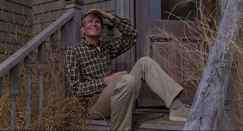 Movie still from “Psycho III” (1986), directed by Anthony Perkins – A man sitting on the steps of a house with his hand on his head; Medium shot, Low angle