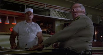 Movie still from “Psycho III” (1986), directed by Anthony Perkins – Two men standing at a counter in front of a counter; Medium shot, Low angle