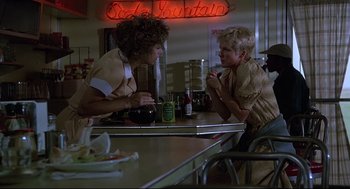 Movie still from “Psycho III” (1986), directed by Anthony Perkins – Two women sitting at a table in front of a neon sign; Medium shot, Low angle