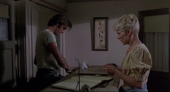 Movie still from “Psycho III” (1986), directed by Anthony Perkins – A man and a woman are looking at papers on a table; Medium shot, Low angle