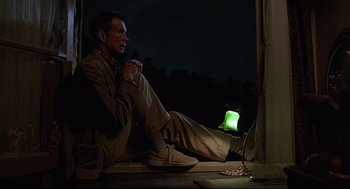 Movie still from “Psycho III” (1986), directed by Anthony Perkins – A man sitting on the ground next to an open laptop computer at night; Medium shot, Low angle