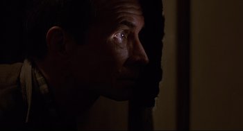 Movie still from “Psycho III” (1986), directed by Anthony Perkins – A person's face with a dark background; Close Up shot, Low angle